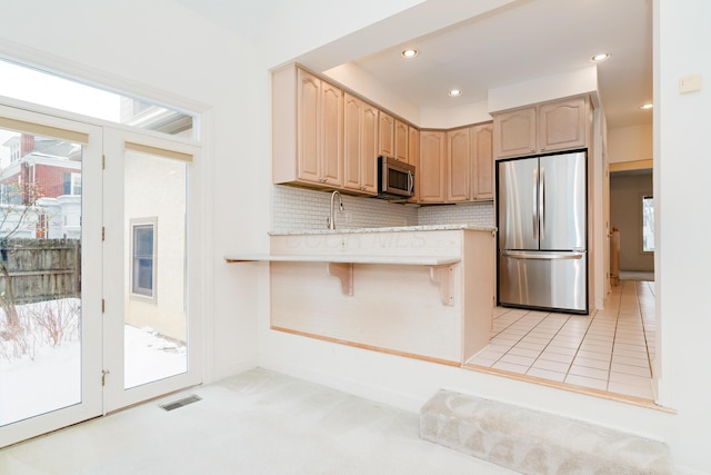 kitchen featuring appliances with stainless steel finishes, decorative backsplash, light brown cabinetry, light colored carpet, and a breakfast bar