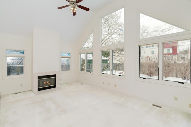 unfurnished living room featuring ceiling fan, high vaulted ceiling, light carpet, and a tiled fireplace