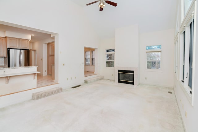 unfurnished living room featuring ceiling fan, light colored carpet, a tile fireplace, and a high ceiling