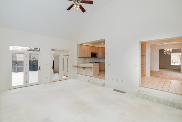 unfurnished living room featuring high vaulted ceiling, light colored carpet, plenty of natural light, and ceiling fan with notable chandelier