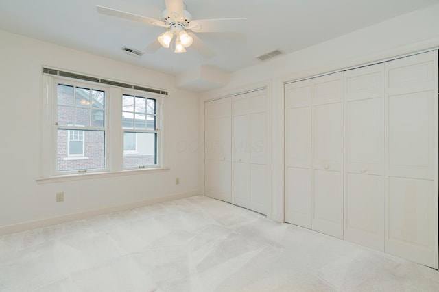 unfurnished bedroom featuring ceiling fan, light colored carpet, and multiple closets