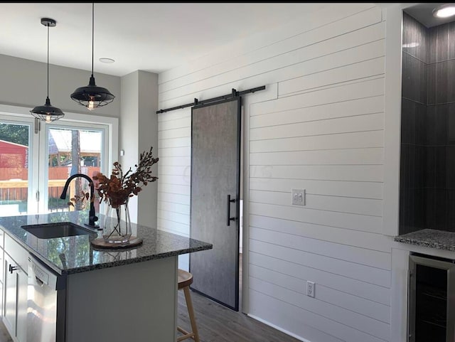 kitchen with hanging light fixtures, beverage cooler, a barn door, dark stone counters, and sink