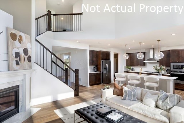 living room with a high end fireplace, a high ceiling, sink, and light wood-type flooring