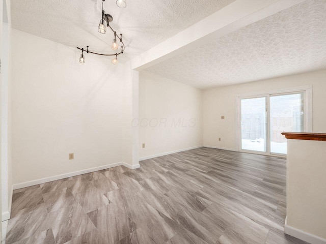 unfurnished dining area featuring a textured ceiling, light wood-type flooring, and rail lighting