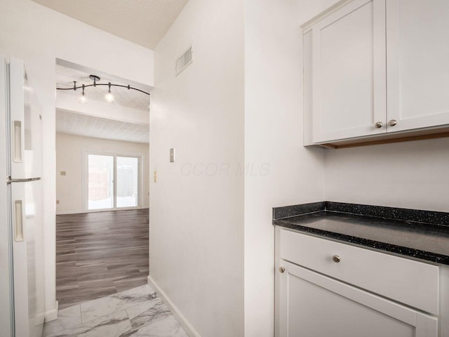 kitchen with white cabinets, white fridge with ice dispenser, and a textured ceiling