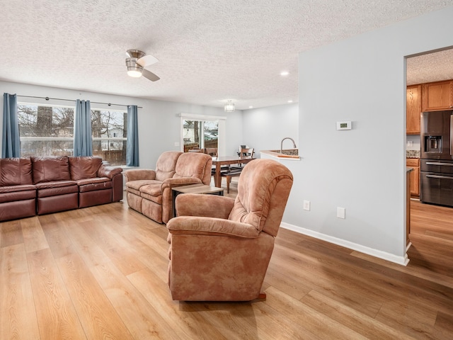 living room with a textured ceiling, ceiling fan, and light hardwood / wood-style floors