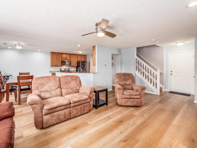 living room featuring a textured ceiling, ceiling fan, and light hardwood / wood-style flooring