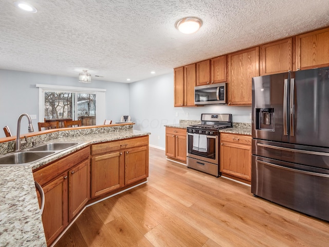 kitchen featuring sink, a textured ceiling, light stone counters, light hardwood / wood-style floors, and appliances with stainless steel finishes