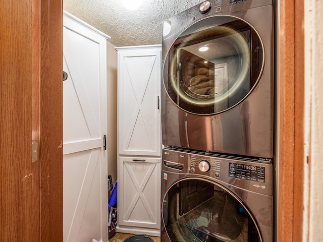 washroom featuring a textured ceiling, cabinets, and stacked washer / drying machine