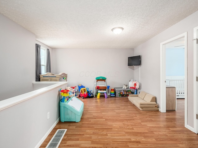 playroom featuring a baseboard heating unit, a textured ceiling, and light hardwood / wood-style flooring