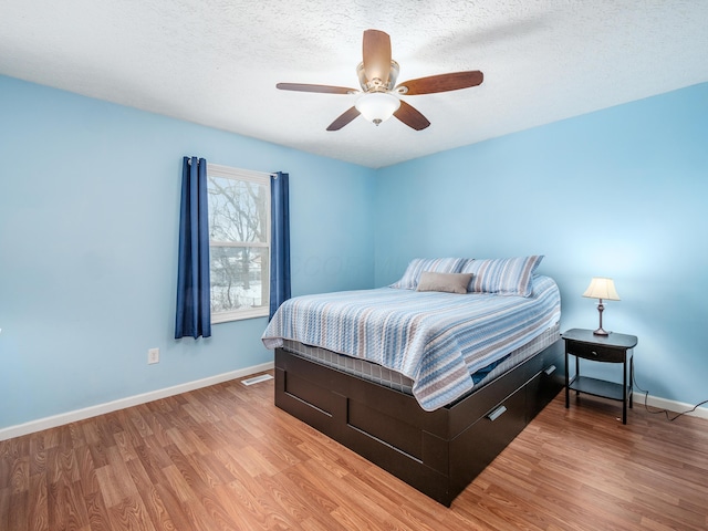 bedroom with a textured ceiling, ceiling fan, and light hardwood / wood-style flooring