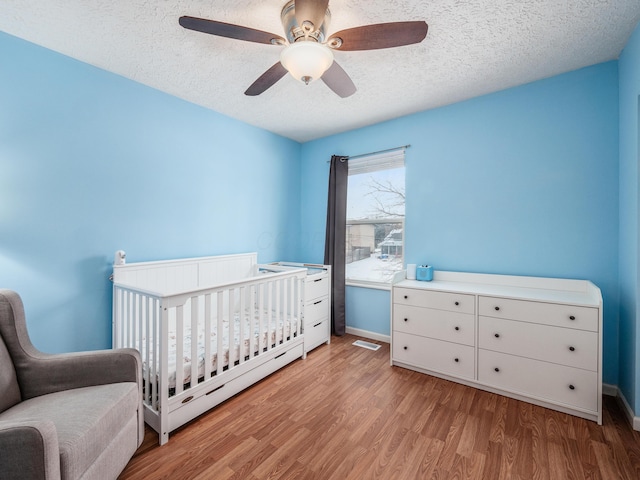 bedroom with light wood-type flooring, a textured ceiling, ceiling fan, and a crib