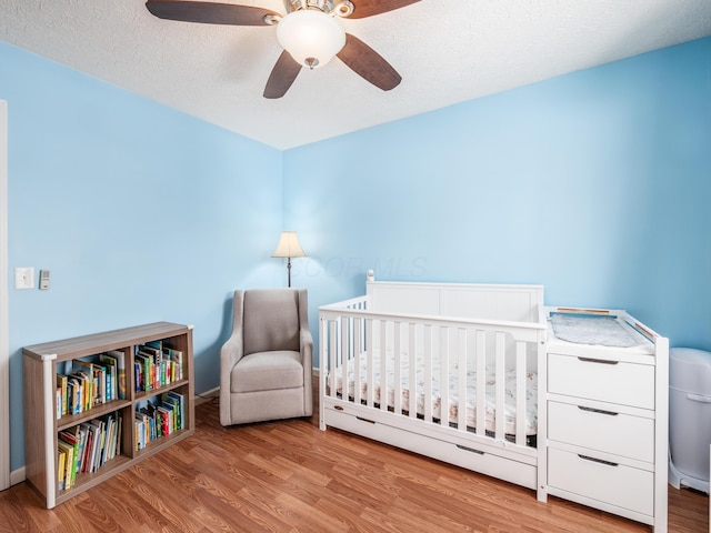 bedroom featuring ceiling fan, light hardwood / wood-style floors, a textured ceiling, and a nursery area