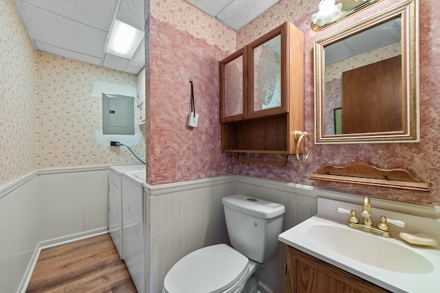 bathroom with independent washer and dryer, toilet, vanity, electric panel, and a drop ceiling