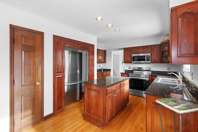 kitchen featuring appliances with stainless steel finishes, light wood-type flooring, a textured ceiling, a kitchen island, and sink