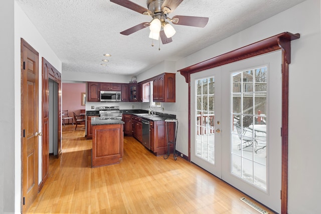 kitchen featuring a kitchen island, light wood-type flooring, appliances with stainless steel finishes, ceiling fan, and sink