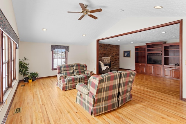 living room with a textured ceiling, lofted ceiling, light wood-type flooring, a fireplace, and ceiling fan