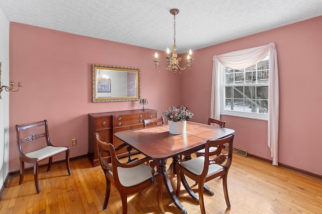 dining space with a notable chandelier, a textured ceiling, and light hardwood / wood-style floors