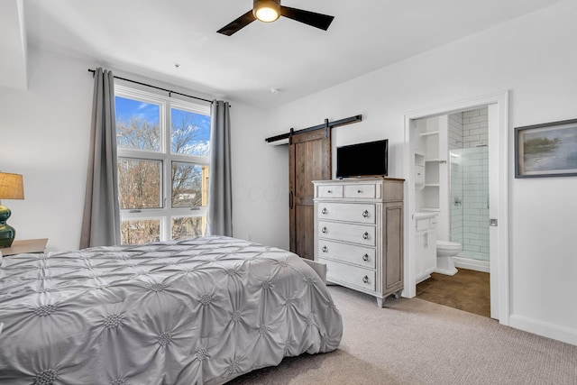 bedroom featuring ceiling fan, ensuite bathroom, light colored carpet, a barn door, and a spacious closet