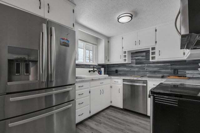 kitchen featuring sink, white cabinetry, a textured ceiling, light wood-type flooring, and appliances with stainless steel finishes