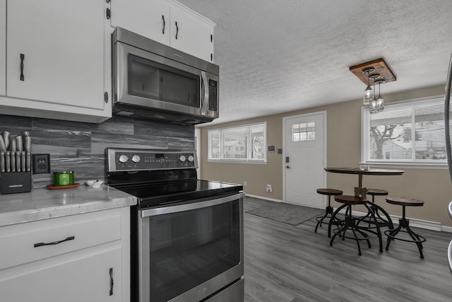 kitchen featuring a textured ceiling, pendant lighting, stainless steel appliances, backsplash, and white cabinets