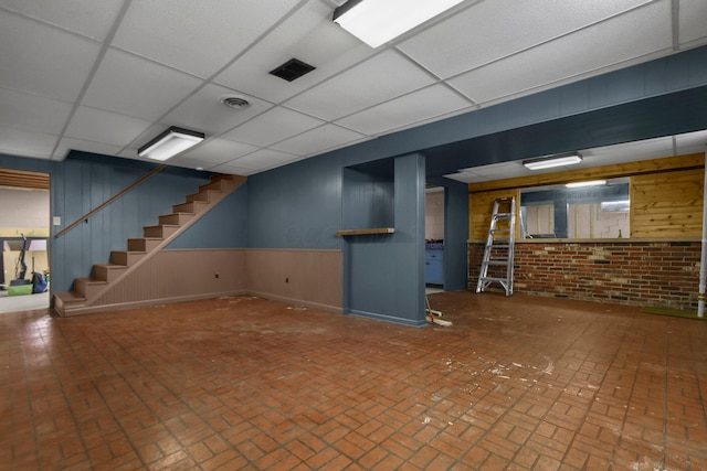 basement with wood walls, brick wall, and a drop ceiling