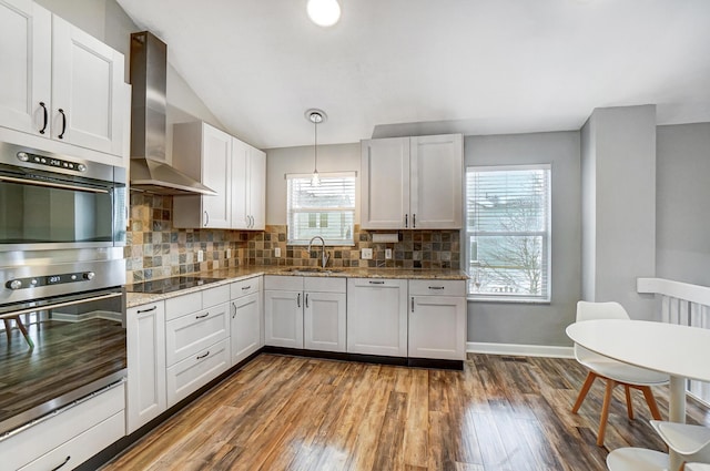 kitchen with wall chimney exhaust hood, decorative light fixtures, white cabinetry, double oven, and sink