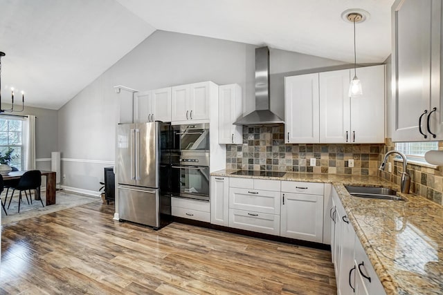 kitchen featuring sink, white cabinets, hanging light fixtures, wall chimney range hood, and appliances with stainless steel finishes