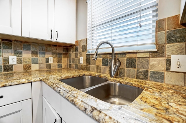 kitchen with light stone countertops, white cabinetry, backsplash, and sink