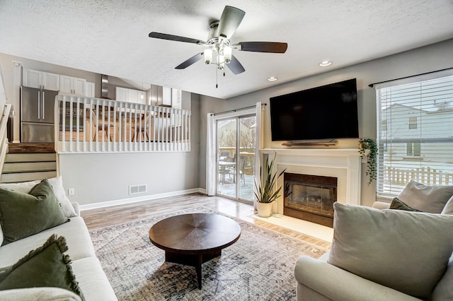 living room featuring a textured ceiling, ceiling fan, and light wood-type flooring