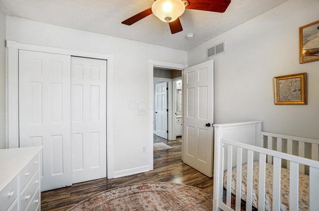 bedroom with a nursery area, ceiling fan, a closet, and dark hardwood / wood-style flooring