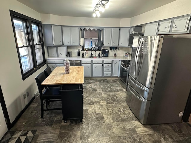 kitchen featuring sink, wooden counters, a kitchen island, gray cabinetry, and appliances with stainless steel finishes