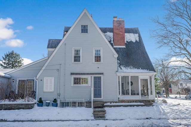 snow covered rear of property with a sunroom