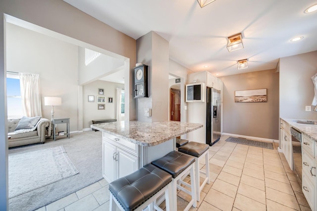 kitchen with stainless steel fridge, a breakfast bar, white cabinetry, and light stone counters