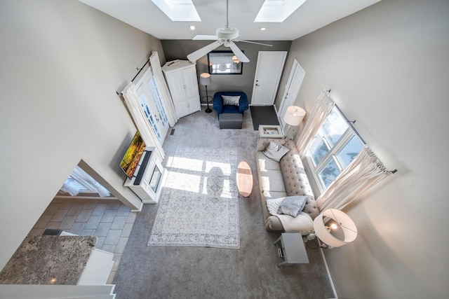 unfurnished living room with a high ceiling, carpet flooring, a skylight, and ceiling fan