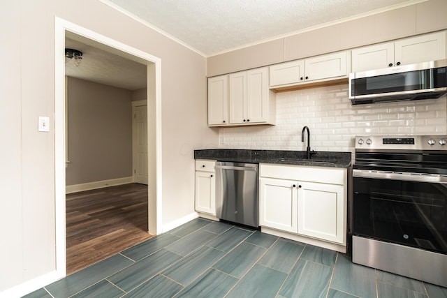 kitchen with a textured ceiling, white cabinets, appliances with stainless steel finishes, dark stone counters, and sink