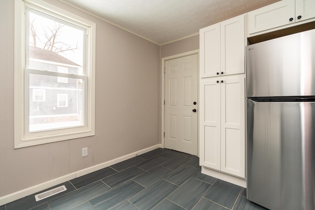 kitchen featuring a textured ceiling, white cabinetry, crown molding, and stainless steel fridge