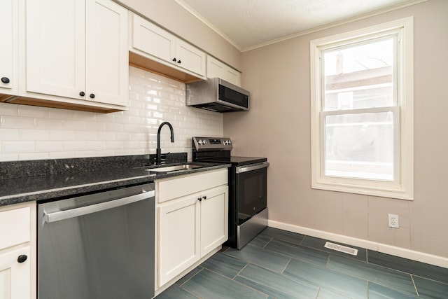 kitchen featuring white cabinetry, stainless steel appliances, dark stone counters, sink, and ornamental molding