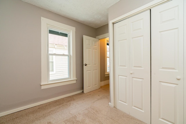 unfurnished bedroom with multiple windows, a textured ceiling, a closet, and light colored carpet