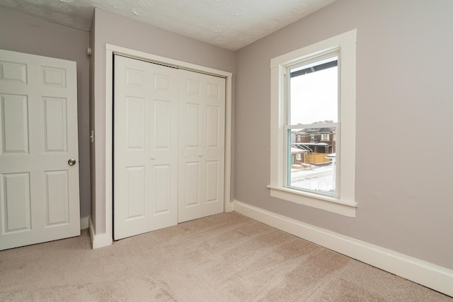 unfurnished bedroom featuring a textured ceiling, a closet, and light carpet