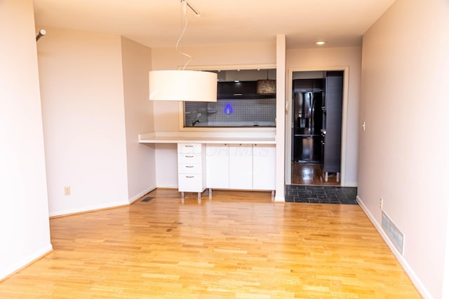 kitchen featuring black fridge, light wood-type flooring, and backsplash