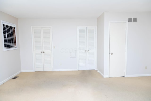 unfurnished bedroom with light colored carpet and two closets