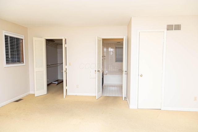 unfurnished bedroom with ensuite bathroom, a closet, light carpet, and a walk in closet