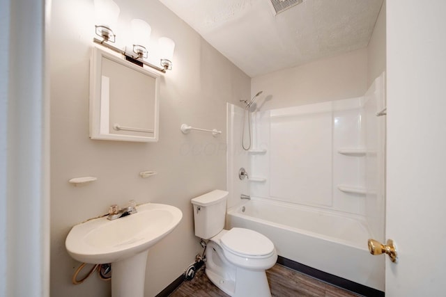 full bathroom featuring toilet, hardwood / wood-style flooring, washtub / shower combination, a textured ceiling, and sink