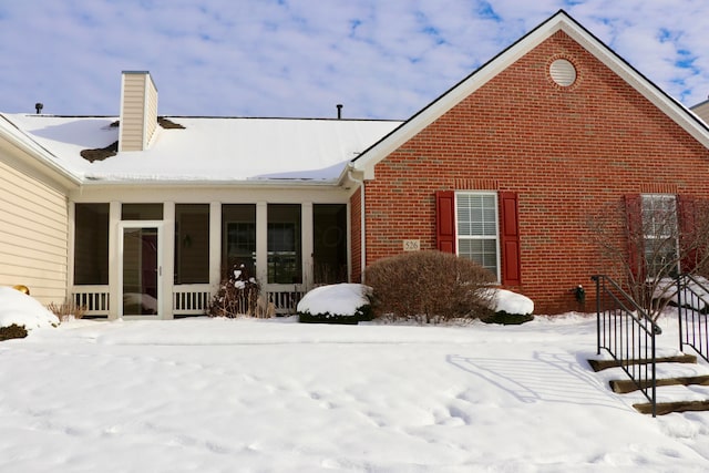 snow covered rear of property featuring a sunroom