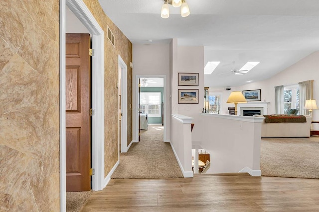 hallway featuring light hardwood / wood-style floors, lofted ceiling with skylight, and a healthy amount of sunlight