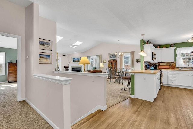 kitchen featuring white cabinetry, kitchen peninsula, decorative light fixtures, vaulted ceiling with skylight, and a breakfast bar