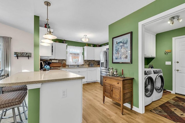 kitchen featuring washer and clothes dryer, kitchen peninsula, stainless steel fridge, pendant lighting, and white cabinets