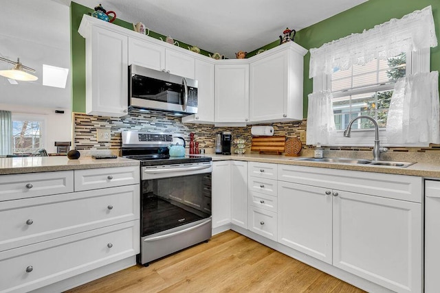 kitchen with a wealth of natural light, sink, a skylight, appliances with stainless steel finishes, and white cabinets