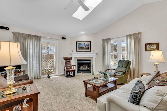 carpeted living room with ceiling fan and vaulted ceiling with skylight